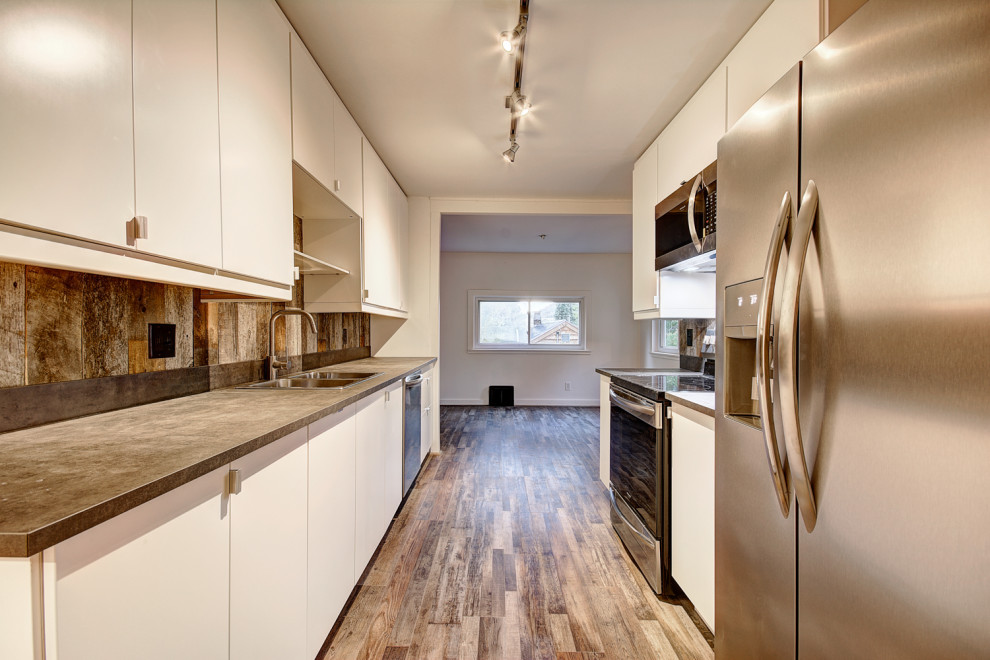 Kitchen - mid-sized rustic galley medium tone wood floor and brown floor kitchen idea in Denver with a drop-in sink, flat-panel cabinets, white cabinets, concrete countertops, brown backsplash, wood backsplash, stainless steel appliances, no island and brown countertops