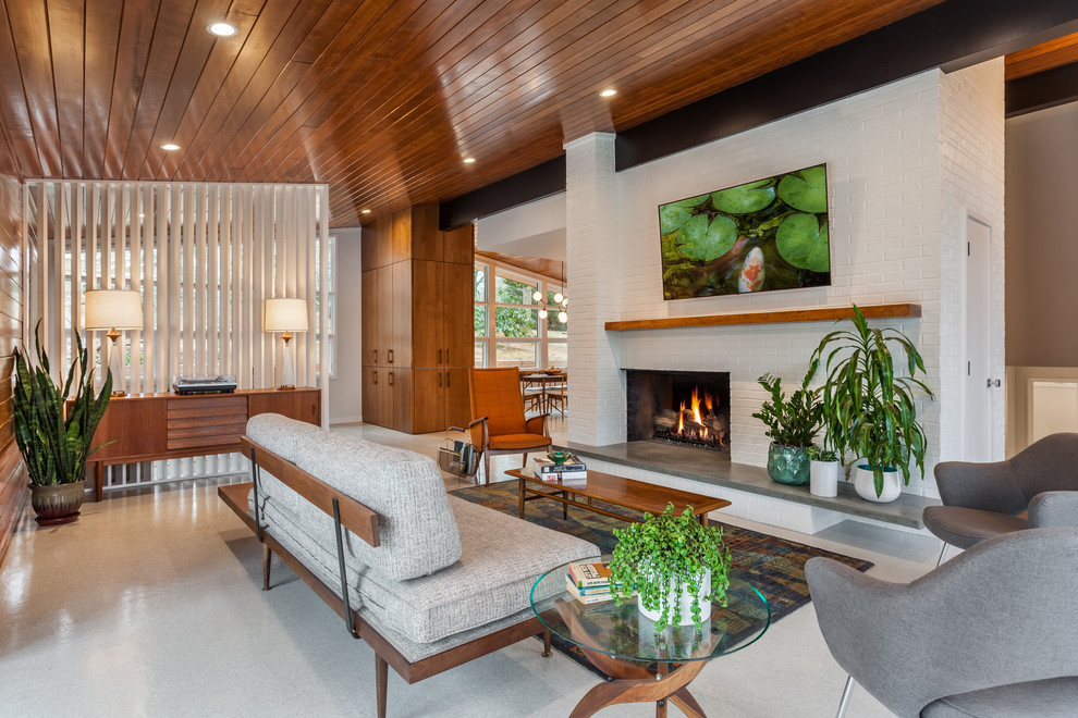 Design ideas for a midcentury open concept living room in Other with white walls, a standard fireplace, a brick fireplace surround, a wall-mounted tv and grey floor.