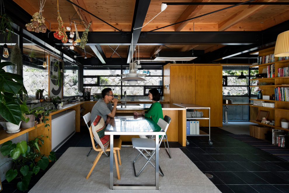 Exempel på ett industriellt grå grått kök, med en integrerad diskho, luckor med profilerade fronter, skåp i ljust trä, bänkskiva i rostfritt stål, fönster som stänkskydd, svarta vitvaror, skiffergolv, en köksö och svart golv
