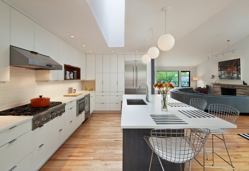 This is an example of a large midcentury u-shaped open plan kitchen in DC Metro with a single-bowl sink, flat-panel cabinets, white cabinets, quartz benchtops, white splashback, ceramic splashback, stainless steel appliances, light hardwood floors, with island and beige floor.