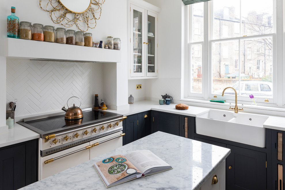 Photo of a small transitional l-shaped eat-in kitchen in London with a farmhouse sink, shaker cabinets, black cabinets, quartzite benchtops, limestone floors, with island and beige floor.