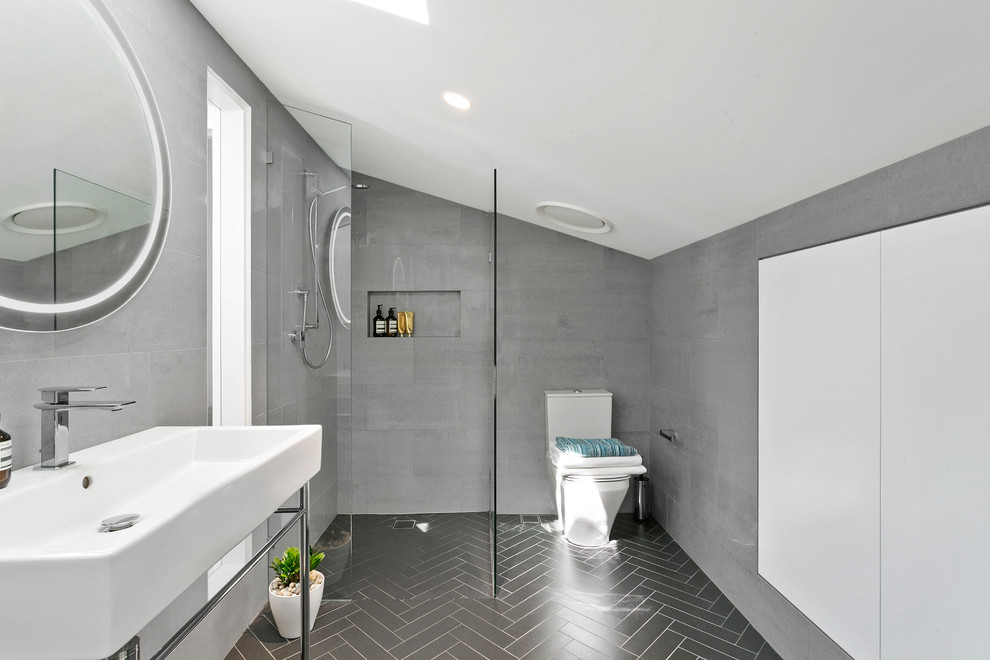 This is an example of a mid-sized contemporary master bathroom in Sydney with recessed-panel cabinets, white cabinets, an open shower, a one-piece toilet, gray tile, ceramic tile, grey walls, ceramic floors, a pedestal sink, grey floor and an open shower.