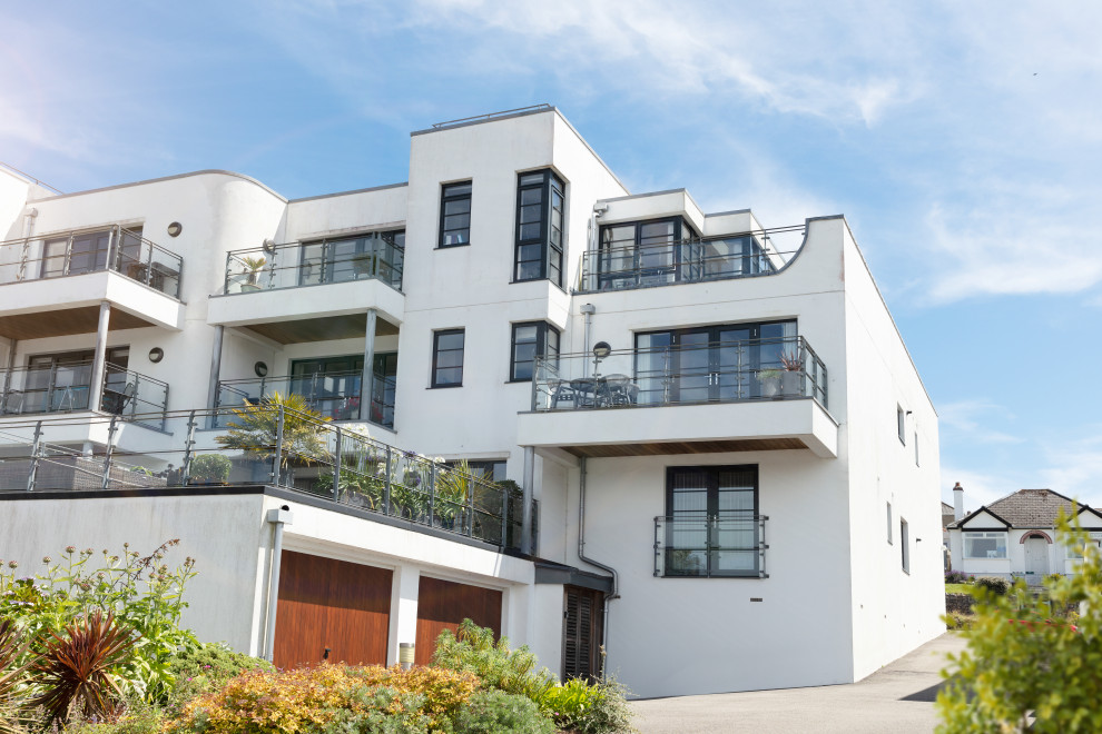 На фото: трехэтажный, белый многоквартирный дом среднего размера в морском стиле с облицовкой из цементной штукатурки, плоской крышей, металлической крышей и серой крышей