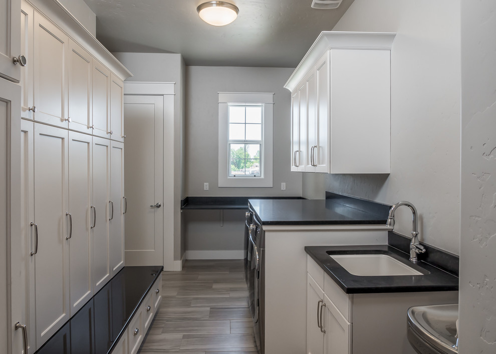 Photo of a mid-sized arts and crafts galley utility room in Boise with an undermount sink, granite benchtops, medium hardwood floors, a side-by-side washer and dryer, shaker cabinets, white cabinets, brown floor and grey walls.
