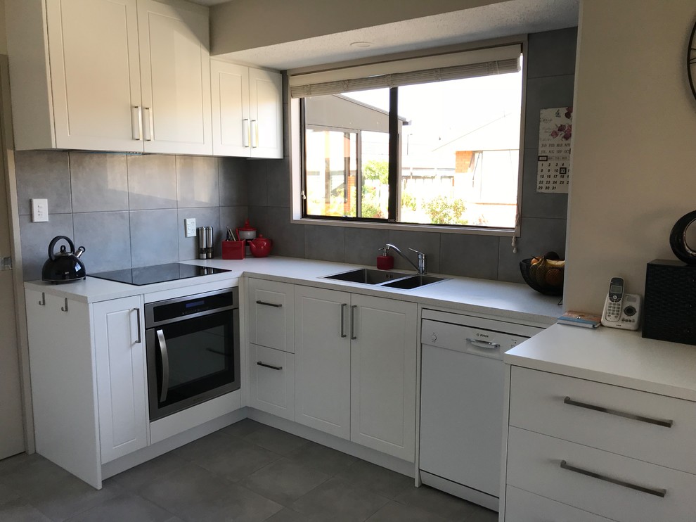 Photo of a mid-sized contemporary galley open plan kitchen in Christchurch with a double-bowl sink, flat-panel cabinets, white cabinets, laminate benchtops, grey splashback, porcelain splashback, stainless steel appliances, porcelain floors, grey floor and white benchtop.