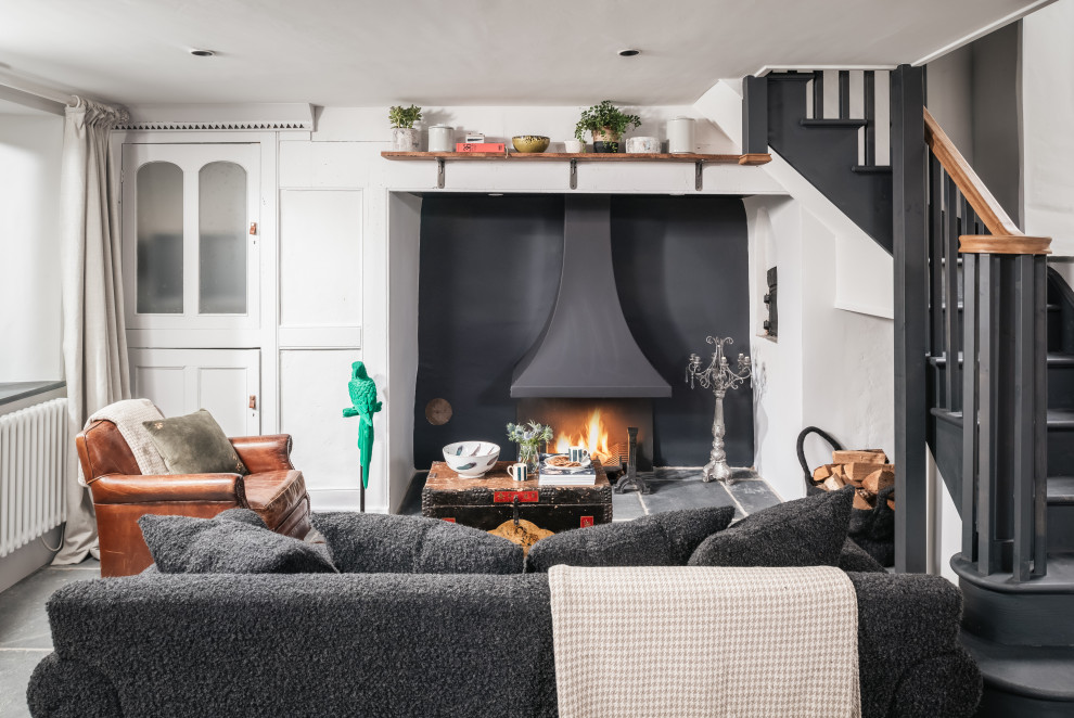 This is an example of a small country open concept living room in Other with a library, grey walls, slate floors, a standard fireplace, a stone fireplace surround, a concealed tv and grey floor.