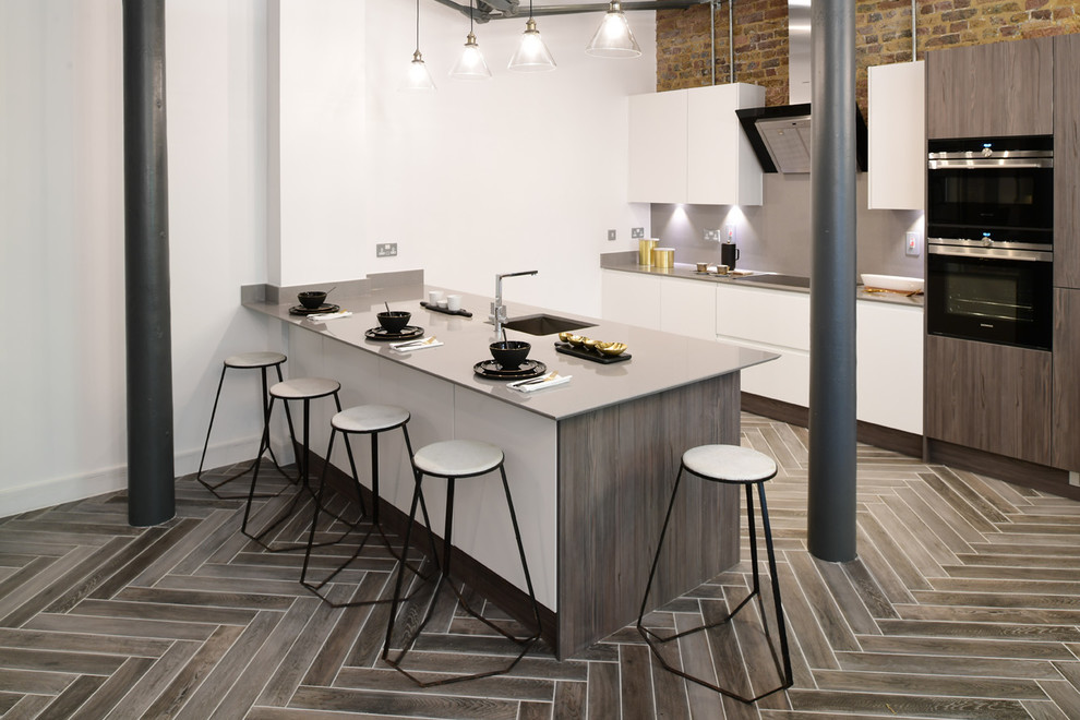 Inspiration for a mid-sized industrial galley kitchen in London with an undermount sink, flat-panel cabinets, grey splashback, white cabinets, black appliances, a peninsula, grey floor and porcelain floors.