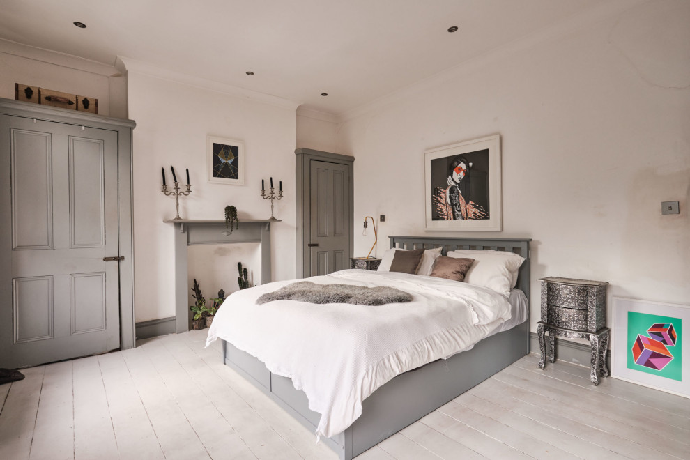 Mittelgroßes Eklektisches Hauptschlafzimmer mit weißer Wandfarbe, gebeiztem Holzboden, Kamin, Kaminumrandung aus Holz und weißem Boden in London