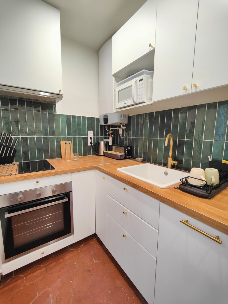 Foto på ett avskilt, litet minimalistiskt l-kök, med en enkel diskho, släta luckor, vita skåp, laminatbänkskiva, grönt stänkskydd, stänkskydd i keramik, rostfria vitvaror, klinkergolv i terrakotta och rött golv