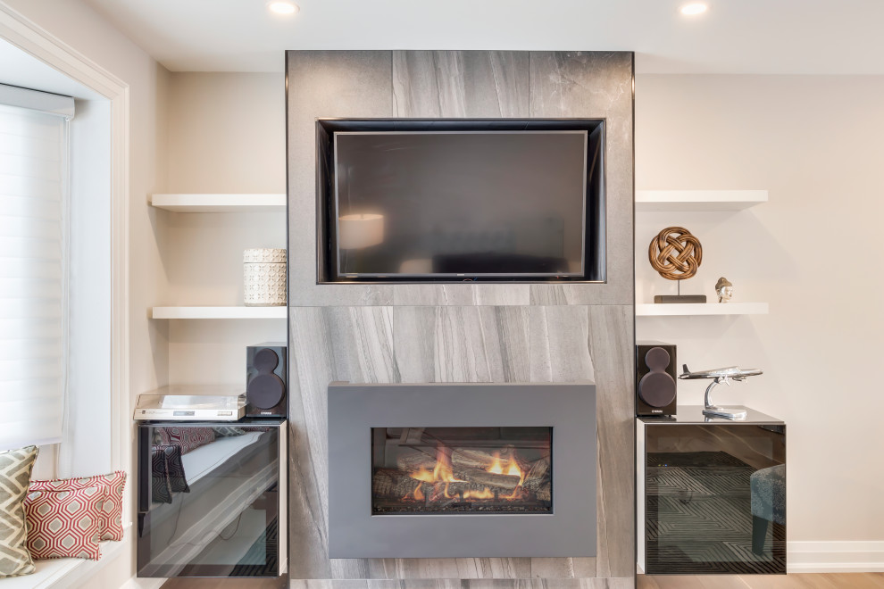 Mid-sized contemporary open concept family room in Toronto with grey walls, medium hardwood floors, a hanging fireplace, a tile fireplace surround, a built-in media wall and brown floor.