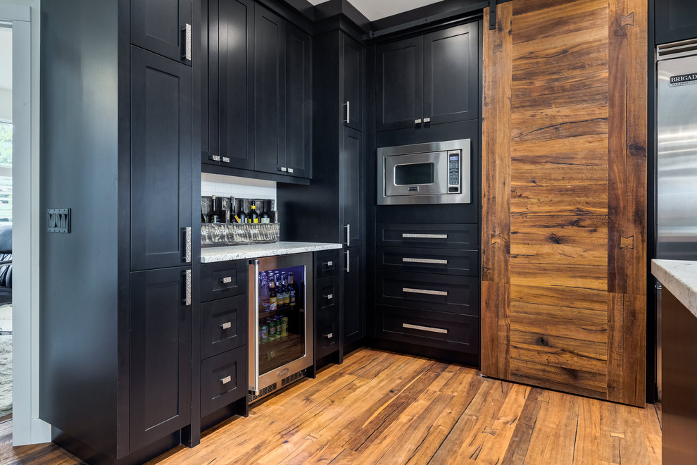 Inspiration for a transitional u-shaped medium tone wood floor and brown floor kitchen remodel in Calgary with an undermount sink, shaker cabinets, black cabinets, quartz countertops, white backsplash, ceramic backsplash, stainless steel appliances and an island