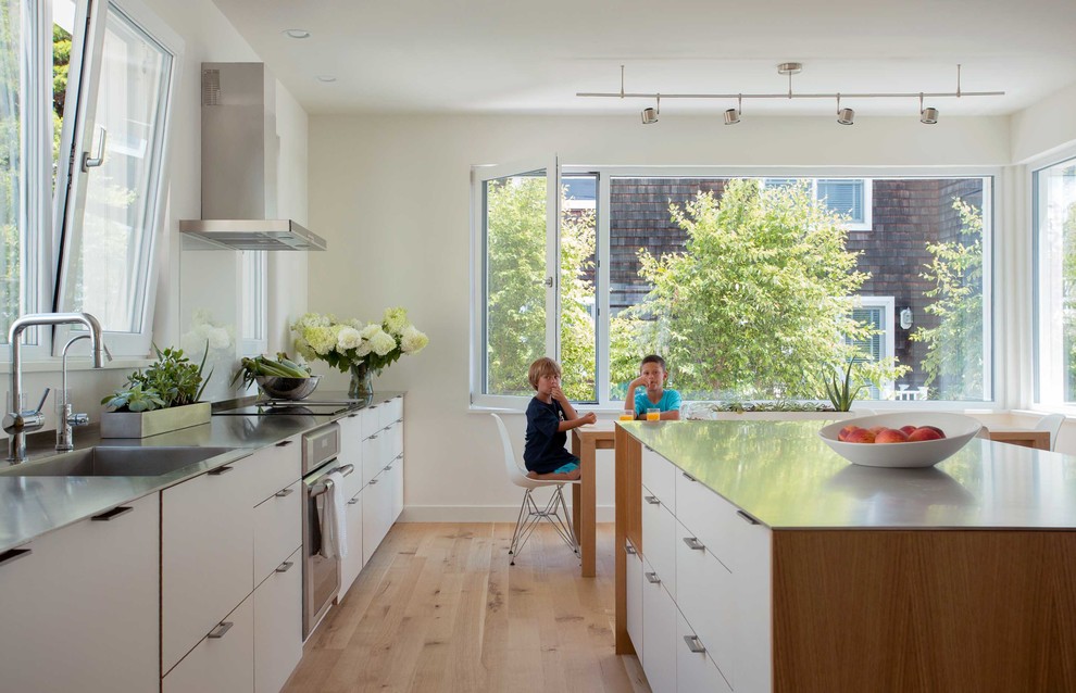 Beach style eat-in kitchen in Newark with an integrated sink, flat-panel cabinets, white cabinets, stainless steel benchtops, stainless steel appliances, light hardwood floors, with island and beige floor.
