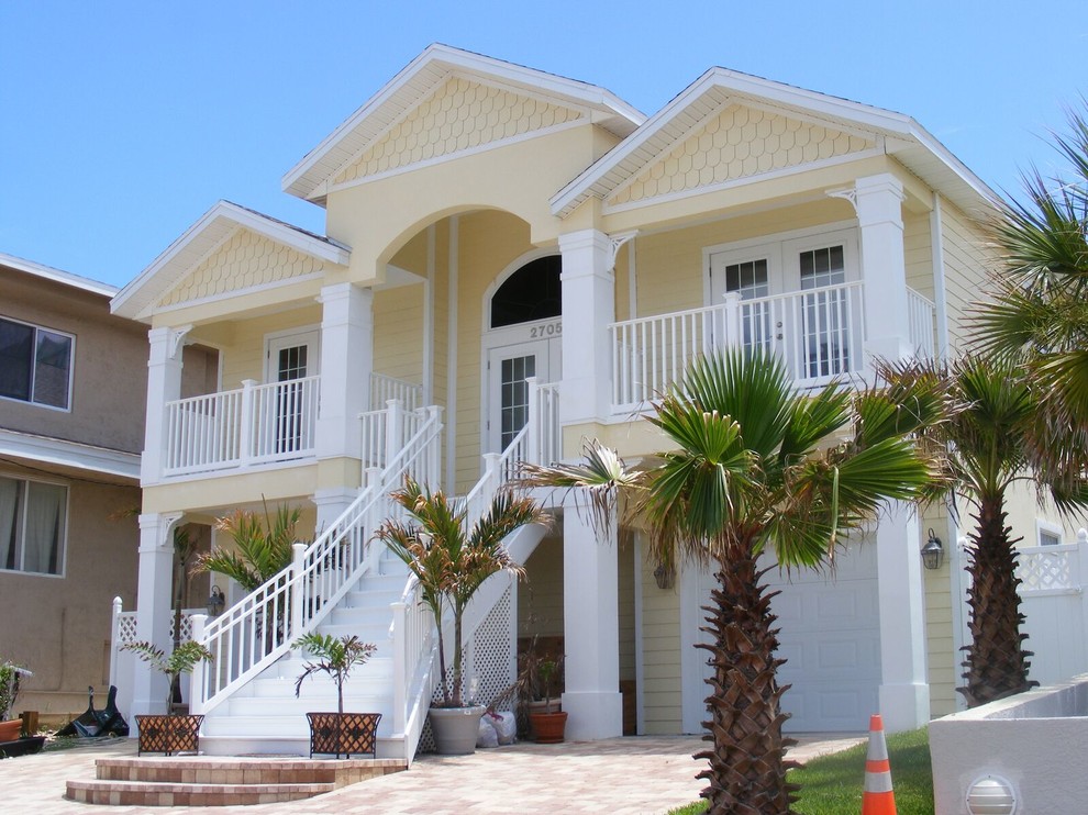 Photo of a large beach style two-storey yellow house exterior in Orlando with wood siding, a hip roof and a shingle roof.