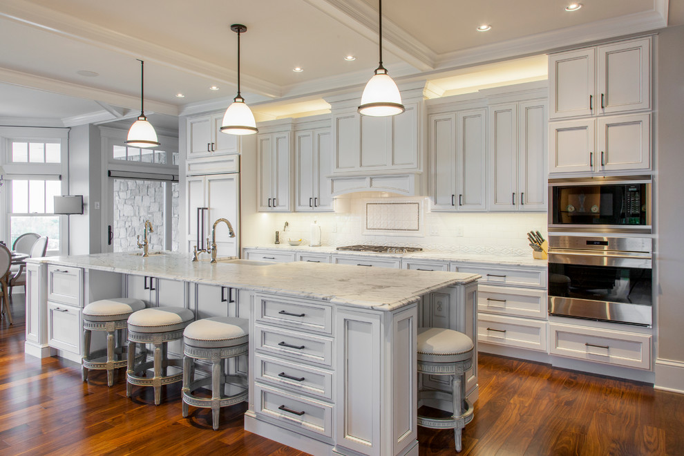 Inspiration for a large arts and crafts galley open plan kitchen in Burlington with a farmhouse sink, recessed-panel cabinets, white cabinets, marble benchtops, white splashback, stone tile splashback, panelled appliances, dark hardwood floors and with island.