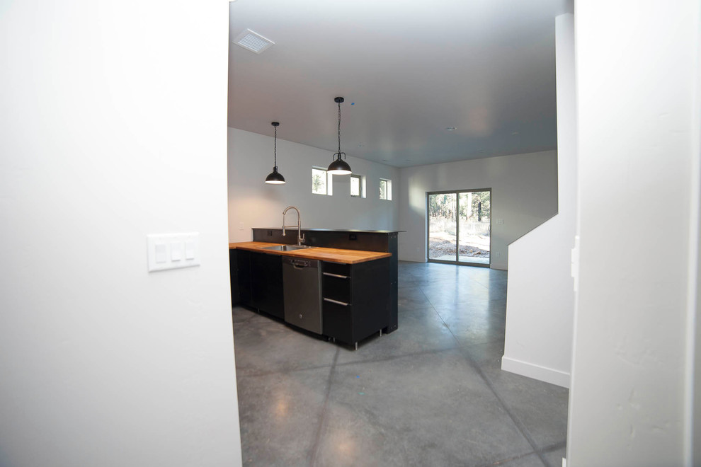 This is an example of a small industrial u-shaped open plan kitchen in Phoenix with a single-bowl sink, flat-panel cabinets, black cabinets, wood benchtops, black splashback, concrete floors and no island.