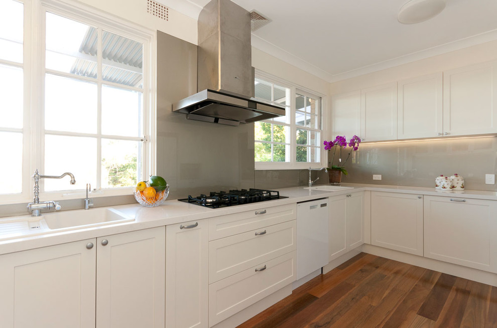 Design ideas for a mid-sized traditional u-shaped kitchen in Sydney with a single-bowl sink, shaker cabinets, white cabinets, quartz benchtops, glass sheet splashback, medium hardwood floors and no island.