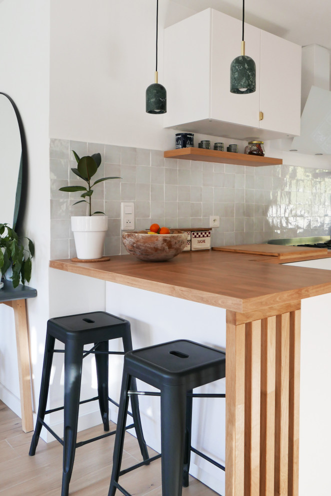 Inspiration for a mid-sized country l-shaped eat-in kitchen in Marseille with flat-panel cabinets, white cabinets, wood benchtops, white splashback, terra-cotta splashback, cement tiles, a peninsula and green floor.