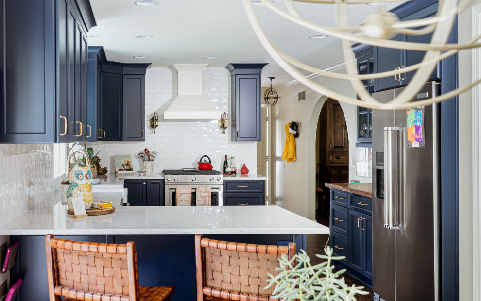 Photo of a small eclectic l-shaped eat-in kitchen in Atlanta with a farmhouse sink, shaker cabinets, blue cabinets, quartz benchtops, blue splashback, ceramic splashback, stainless steel appliances, medium hardwood floors, a peninsula, brown floor and blue benchtop.