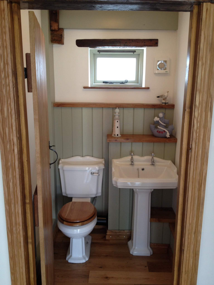 Photo of a small traditional 3/4 bathroom in Cambridgeshire with glass-front cabinets, medium wood cabinets, a curbless shower, a one-piece toilet, stone tile, green walls, dark hardwood floors, a pedestal sink, wood benchtops, a hinged shower door, brown benchtops, a shower seat, a built-in vanity, exposed beam and panelled walls.