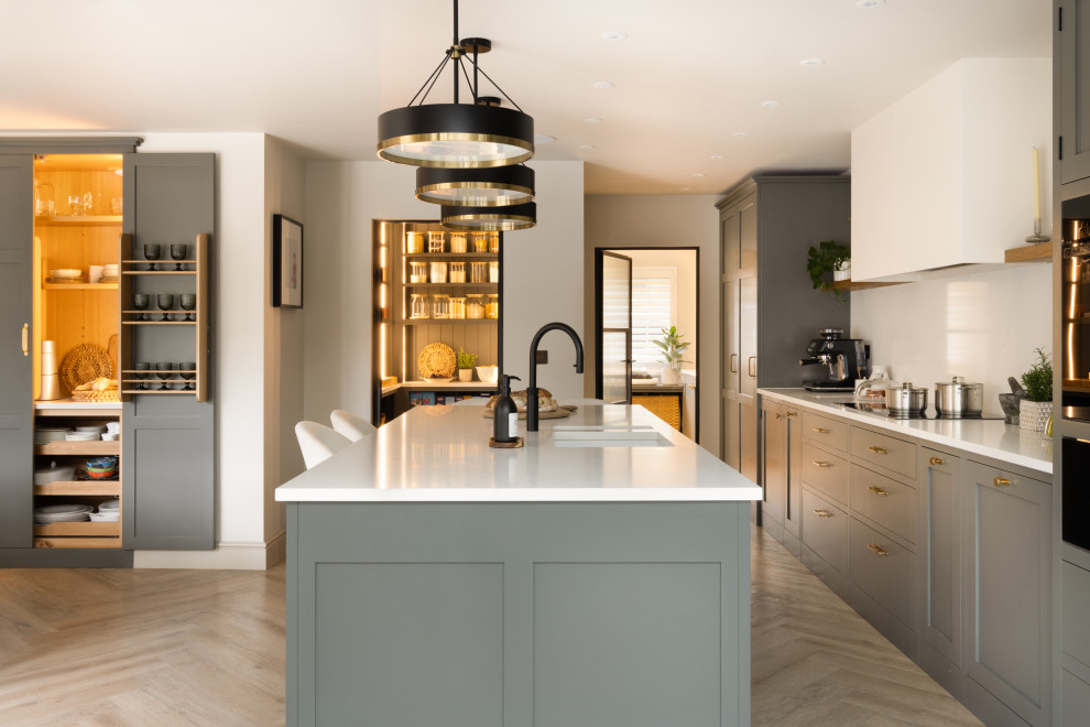 Medium sized traditional single-wall kitchen/diner in London with a submerged sink, shaker cabinets, quartz worktops, white splashback, engineered quartz splashback, integrated appliances, medium hardwood flooring, an island and white worktops.