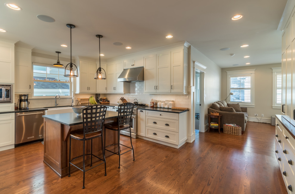 Photo of a mid-sized country u-shaped open plan kitchen in Chicago with shaker cabinets, white cabinets, solid surface benchtops, white splashback, porcelain splashback, stainless steel appliances, medium hardwood floors, with island, brown floor, black benchtop, wallpaper and a drop-in sink.