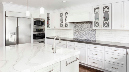 Large transitional u-shaped medium tone wood floor and brown floor enclosed kitchen photo with shaker cabinets, white cabinets, gray backsplash, stainless steel appliances, an island, an undermount sink, marble countertops, subway tile backsplash and white countertops