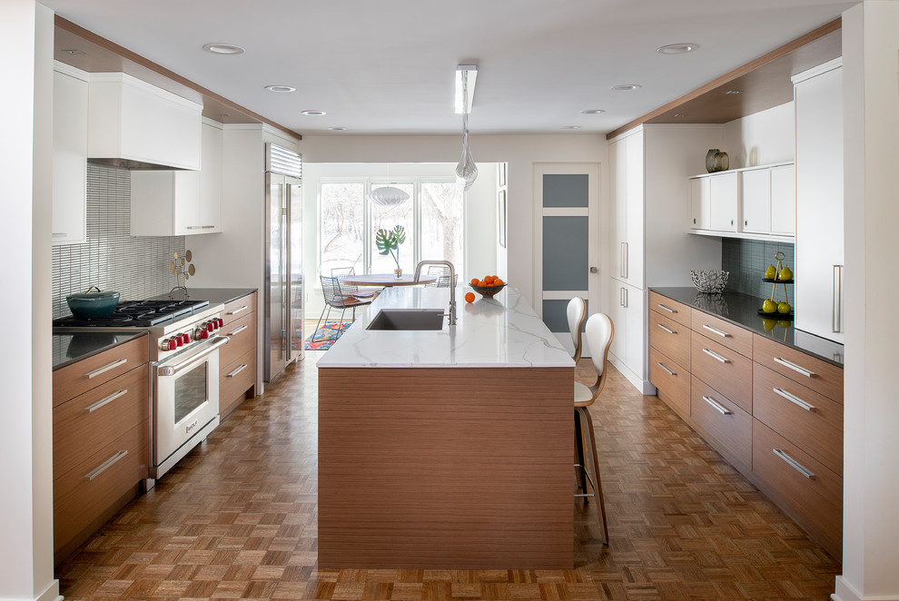 This is an example of a mid-sized midcentury galley eat-in kitchen in Minneapolis with an undermount sink, flat-panel cabinets, quartz benchtops, grey splashback, stainless steel appliances, with island, brown floor, medium wood cabinets, medium hardwood floors and black benchtop.