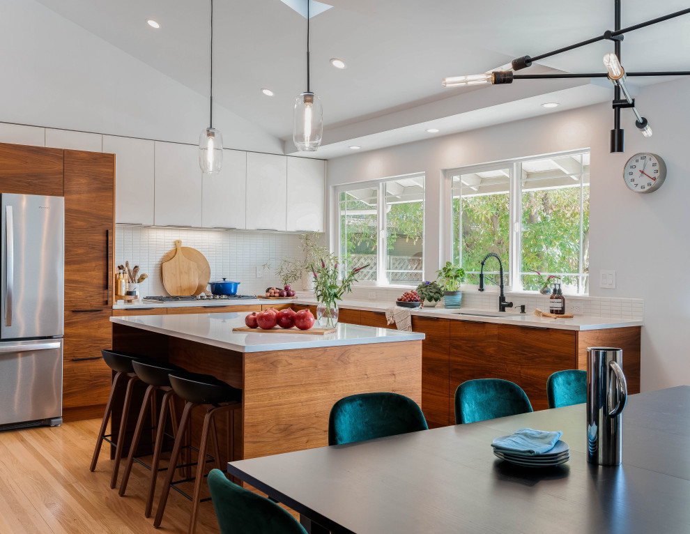 Photo of a mid-sized modern l-shaped eat-in kitchen with an undermount sink, flat-panel cabinets, medium wood cabinets, quartz benchtops, white splashback, ceramic splashback, stainless steel appliances, medium hardwood floors, with island, brown floor, white benchtop and vaulted.