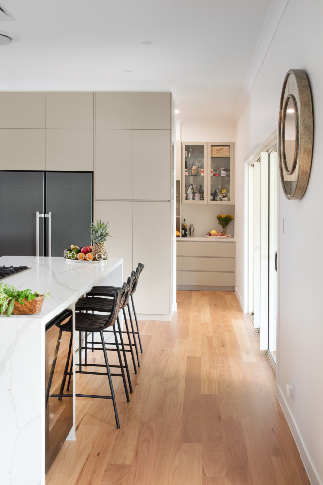 Photo of an expansive modern galley eat-in kitchen in Brisbane with an undermount sink, beige cabinets, quartz benchtops, stainless steel appliances, light hardwood floors, multiple islands and white benchtop.