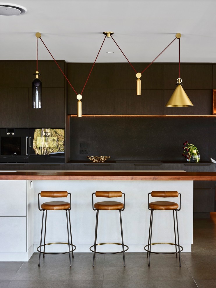 This is an example of a large contemporary galley kitchen in Brisbane with flat-panel cabinets, dark wood cabinets, black splashback, black appliances, with island, black benchtop and grey floor.