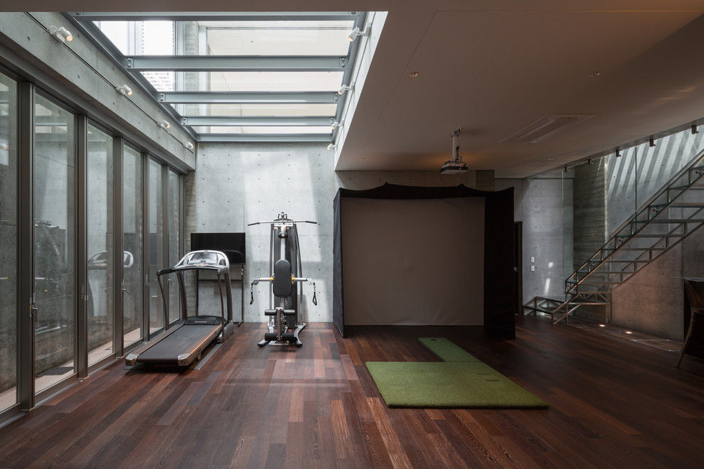 Cette photo montre une très grande salle de musculation tendance avec un mur gris, parquet foncé et un sol marron.