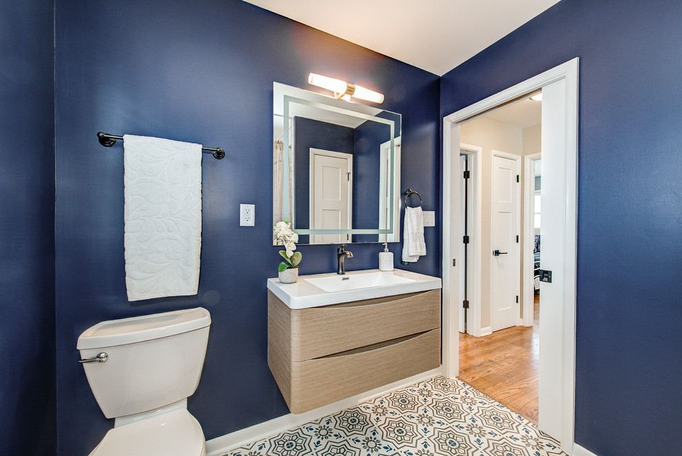Design ideas for a mid-sized contemporary 3/4 bathroom in Indianapolis with flat-panel cabinets, light wood cabinets, a two-piece toilet, blue walls, ceramic floors, an integrated sink, engineered quartz benchtops, multi-coloured floor and white benchtops.