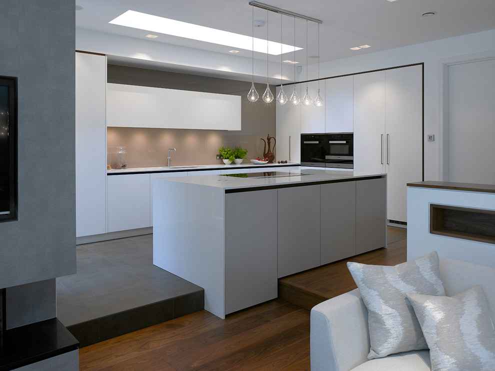 Expansive contemporary open plan kitchen in London with flat-panel cabinets, white cabinets, solid surface benchtops, beige splashback, glass sheet splashback, with island and white benchtop.