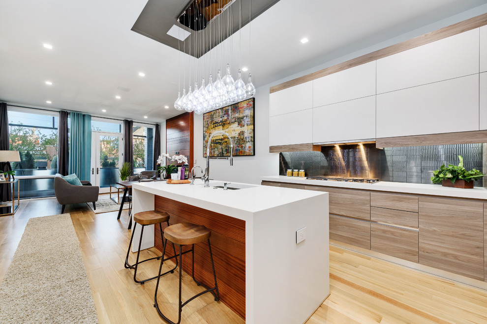 Design ideas for a contemporary galley open plan kitchen in Chicago with an undermount sink, flat-panel cabinets, white cabinets, metallic splashback, metal splashback, panelled appliances, light hardwood floors, with island, beige floor and white benchtop.