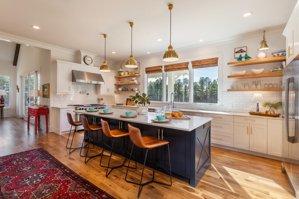 Photo of a large country u-shaped eat-in kitchen in Other with a farmhouse sink, white splashback, ceramic splashback, stainless steel appliances, medium hardwood floors, with island, brown floor, white benchtop, shaker cabinets, blue cabinets and quartz benchtops.