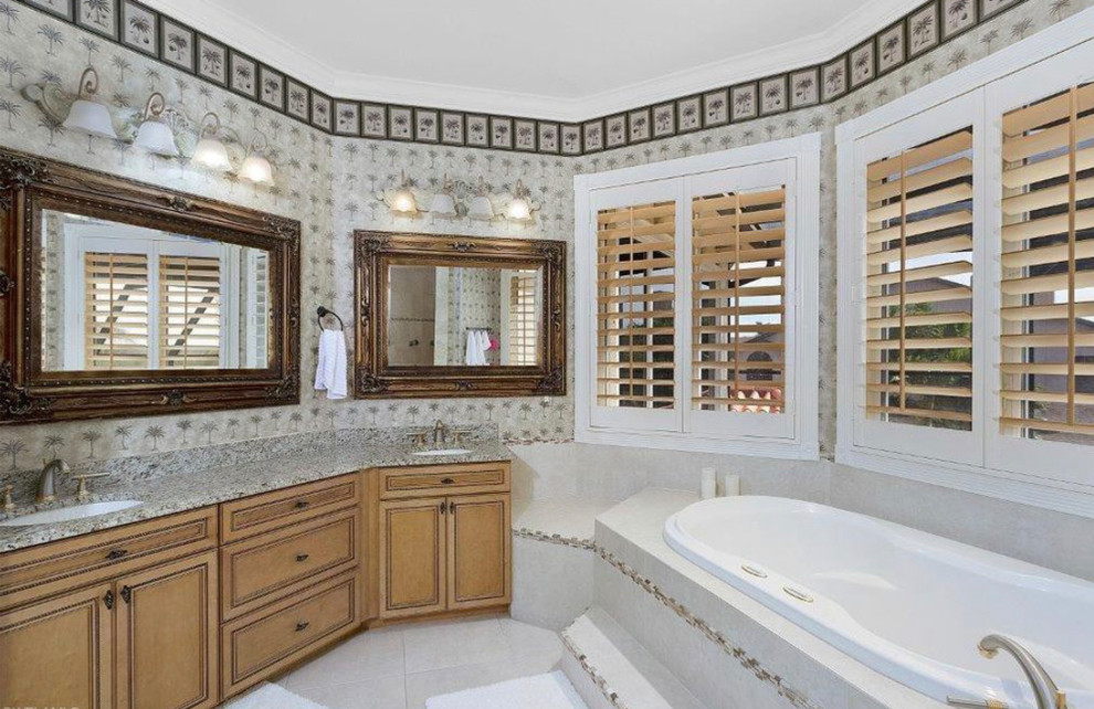 Photo of a large tropical master bathroom in Miami with beaded inset cabinets, medium wood cabinets, a drop-in tub, beige tile, travertine, marble benchtops, beige benchtops, an alcove shower, a two-piece toilet, beige walls, terrazzo floors, a drop-in sink, beige floor and an open shower.