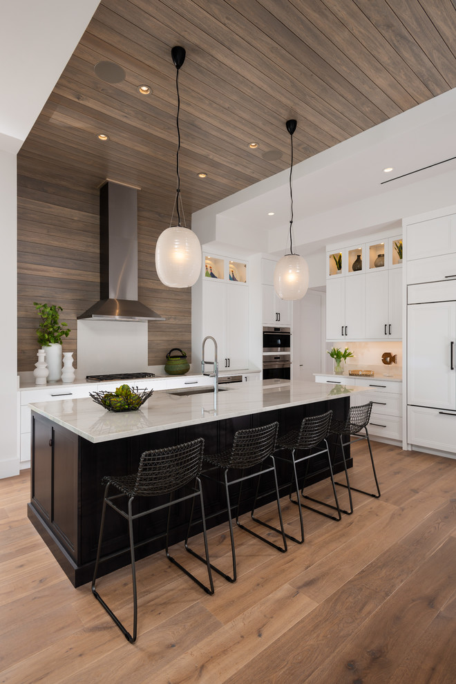 Design ideas for a transitional u-shaped kitchen in Miami with an undermount sink, shaker cabinets, white cabinets, white appliances, medium hardwood floors, with island and brown floor.