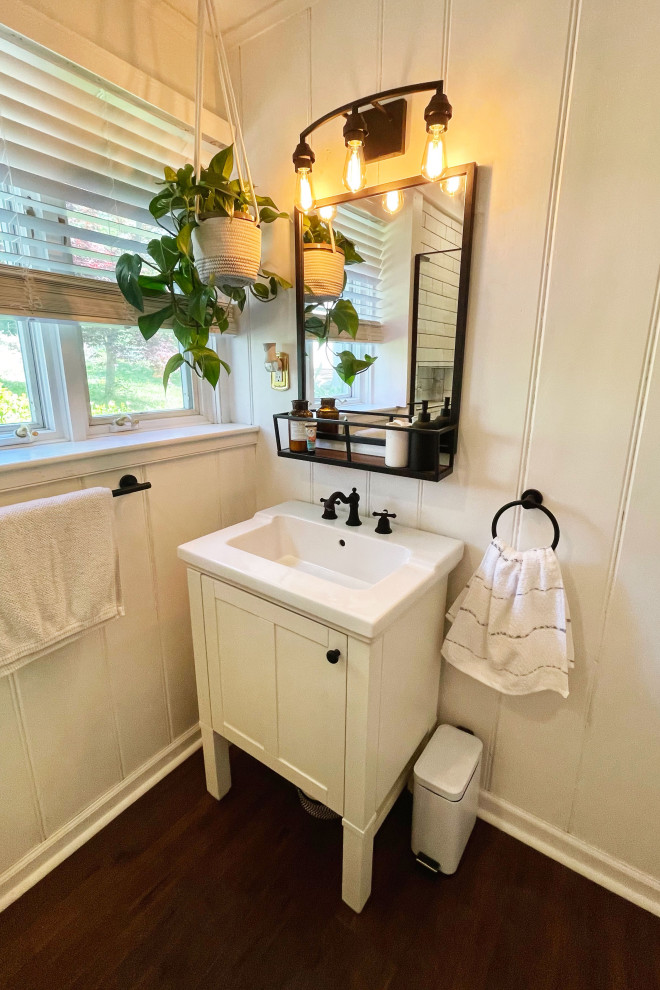 Example of a small farmhouse 3/4 white tile and ceramic tile laminate floor, brown floor, single-sink and wall paneling corner shower design in New York with shaker cabinets, white cabinets, a two-piece toilet, white walls, a drop-in sink, solid surface countertops, a hinged shower door, a niche and a freestanding vanity