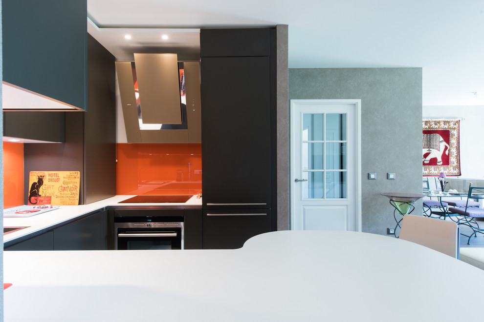 This is an example of a mid-sized tropical u-shaped open plan kitchen in Paris with an integrated sink, beaded inset cabinets, brown cabinets, solid surface benchtops, orange splashback, glass tile splashback, panelled appliances, ceramic floors and a peninsula.