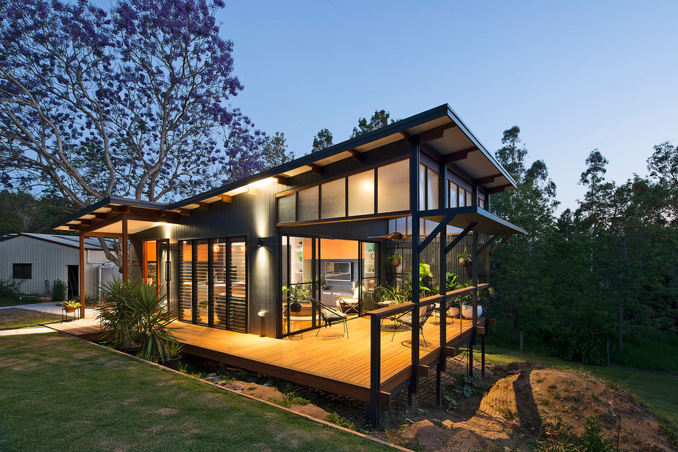 This is an example of a small modern one-storey black house exterior in Brisbane with concrete fiberboard siding, a flat roof and a metal roof.