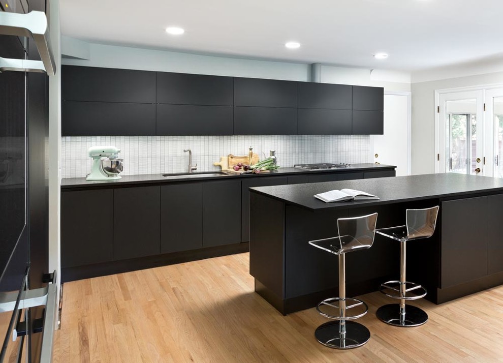 Photo of a mid-sized transitional eat-in kitchen in Detroit with an undermount sink, glass-front cabinets, black cabinets, granite benchtops, white splashback, ceramic splashback, panelled appliances, light hardwood floors and with island.