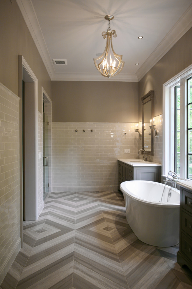 Photo of a large contemporary master bathroom in Atlanta with a freestanding tub, beige walls, recessed-panel cabinets, grey cabinets, an undermount sink, marble benchtops, gray tile, stone tile and limestone floors.
