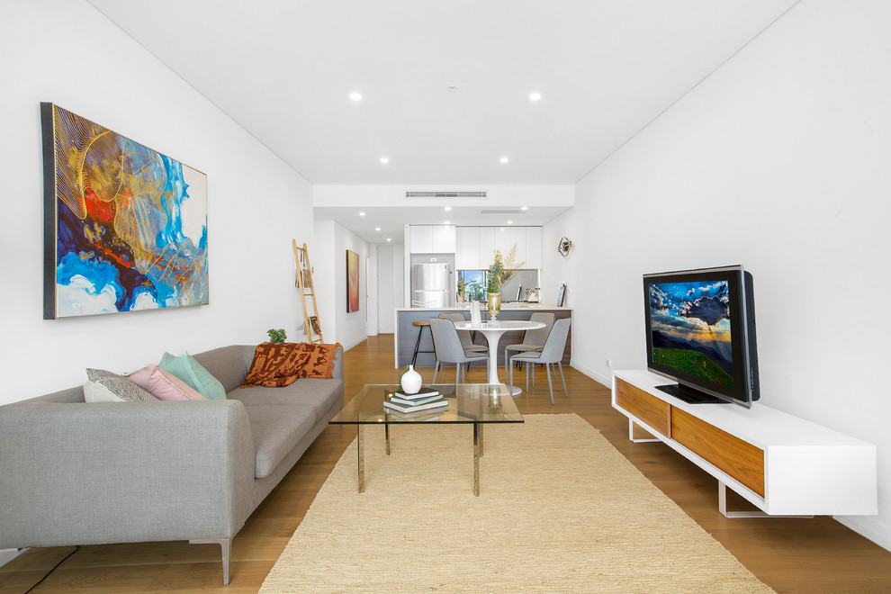 Photo of a modern open concept living room in Sydney with white walls, medium hardwood floors, a freestanding tv and brown floor.