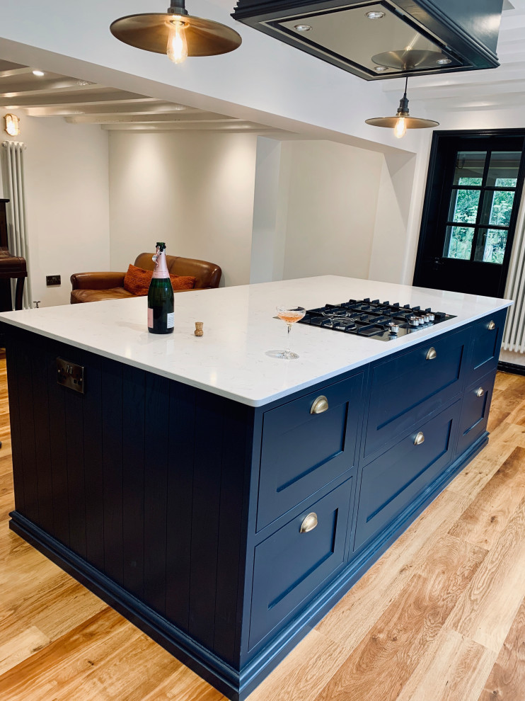 This is an example of a large contemporary l-shaped eat-in kitchen in Other with a farmhouse sink, shaker cabinets, blue cabinets, quartzite benchtops, black appliances, medium hardwood floors, with island, blue floor and white benchtop.
