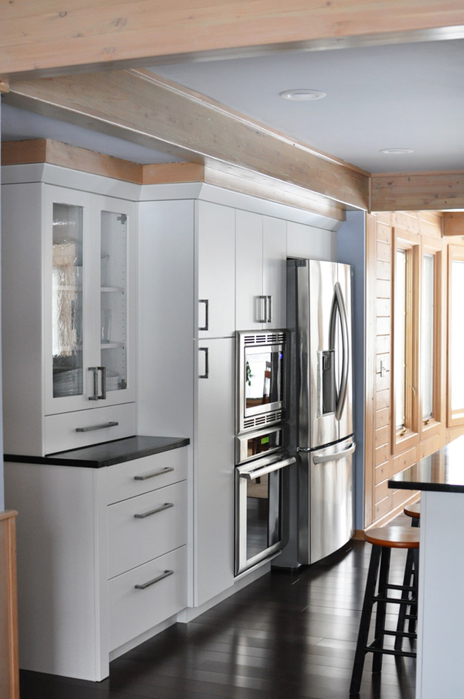 Mid-sized transitional l-shaped dark wood floor eat-in kitchen photo in Grand Rapids with an undermount sink, flat-panel cabinets, white cabinets, soapstone countertops, white backsplash, subway tile backsplash, stainless steel appliances and an island