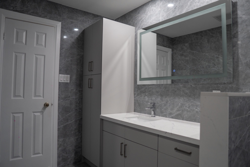 This is an example of a mid-sized modern master bathroom in Toronto with shaker cabinets, white cabinets, a freestanding tub, a curbless shower, a one-piece toilet, gray tile, porcelain tile, grey walls, porcelain floors, an undermount sink, engineered quartz benchtops, grey floor, a sliding shower screen, white benchtops, a niche, a double vanity and a built-in vanity.
