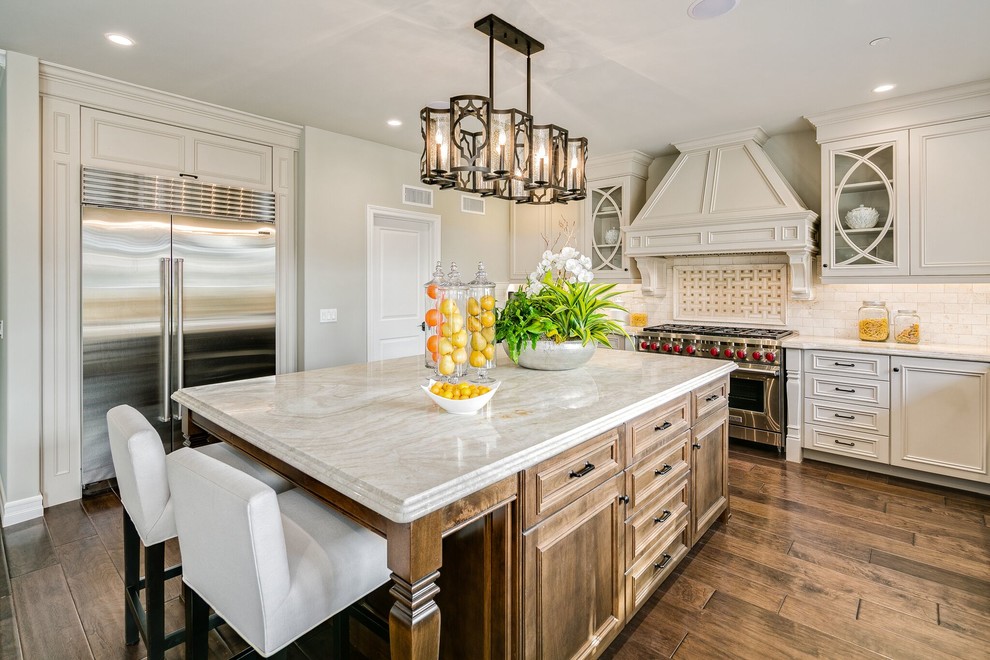 Large traditional l-shaped open plan kitchen in Orange County with dark hardwood floors, brown floor, an undermount sink, recessed-panel cabinets, beige cabinets, limestone benchtops, beige splashback, subway tile splashback, stainless steel appliances and with island.