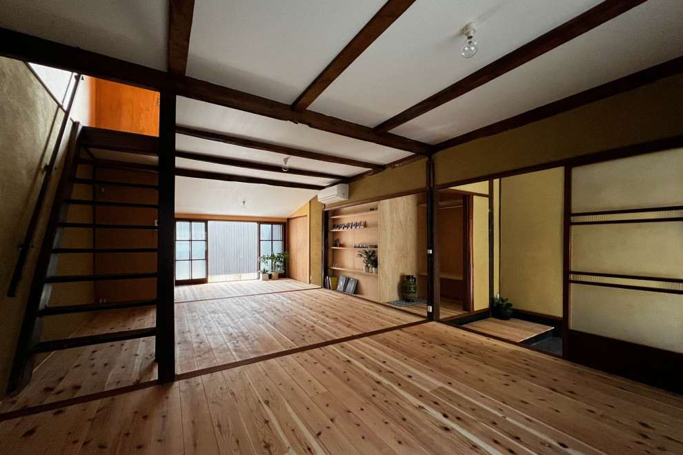京都にある小さな和モダンなおしゃれなオープンリビング (茶色い壁、淡色無垢フローリング、茶色い床、表し梁、アクセントウォール、白い天井) の写真