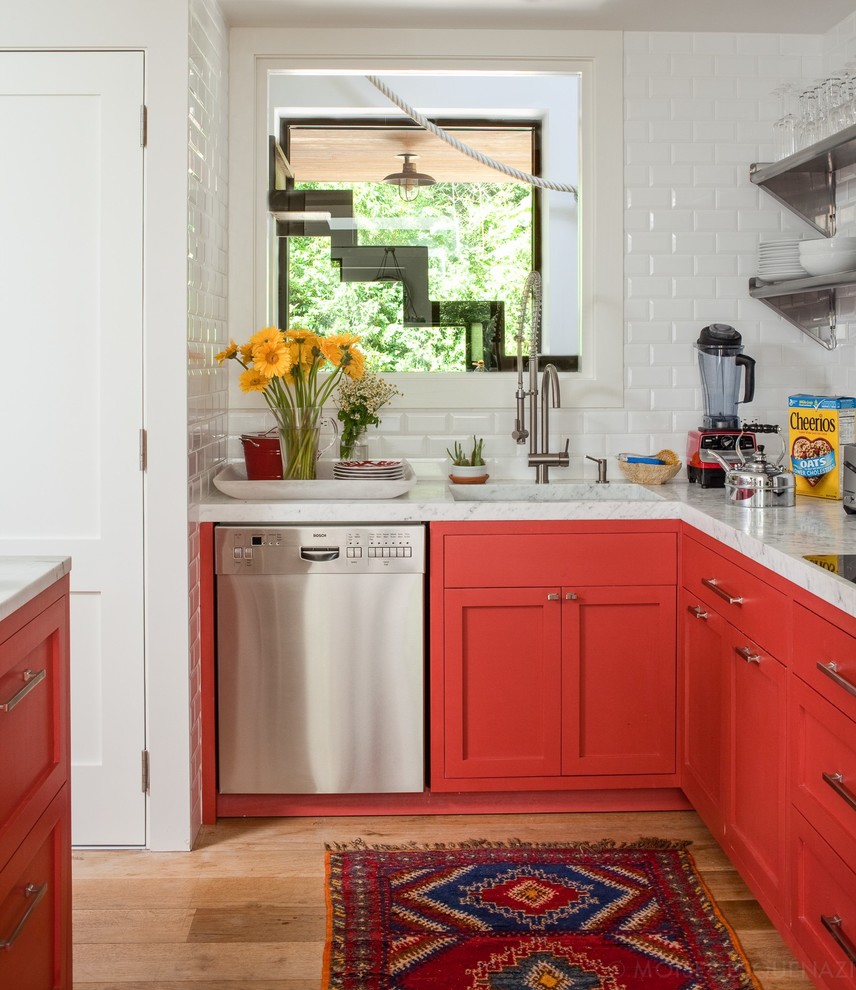 This is an example of a small beach style l-shaped kitchen in New York with a single-bowl sink, shaker cabinets, red cabinets, white splashback, subway tile splashback, stainless steel appliances, light hardwood floors and multi-coloured benchtop.