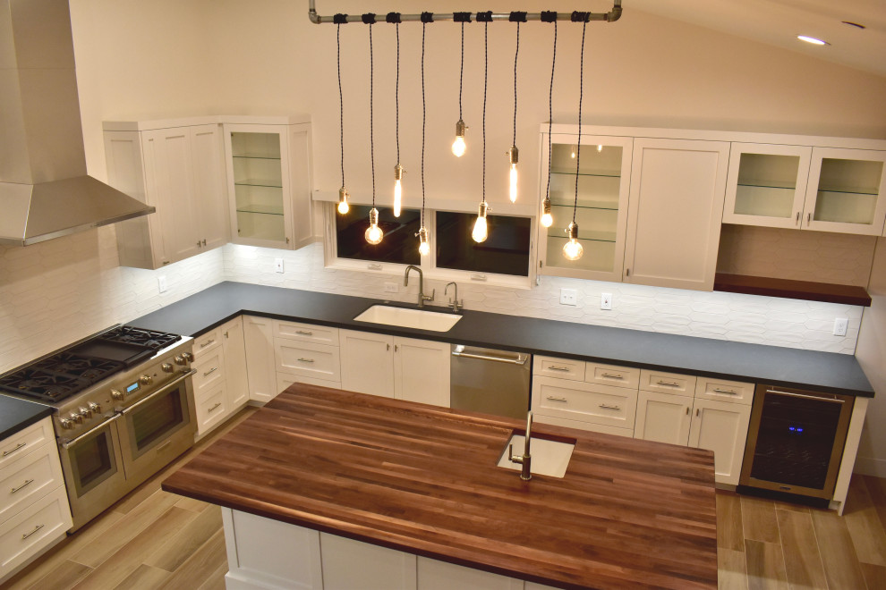Inspiration for a large modern l-shaped eat-in kitchen remodel with an undermount sink, shaker cabinets, white cabinets, quartz countertops, white backsplash, ceramic backsplash, stainless steel appliances, an island and black countertops